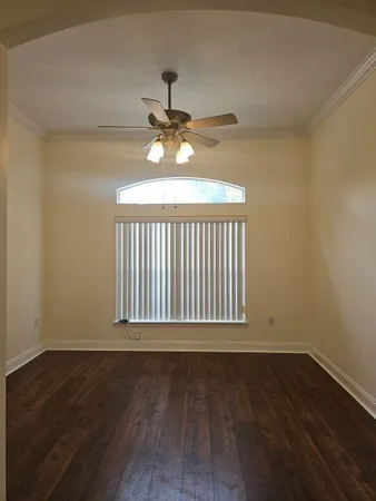 a view of an empty room with wooden floor a ceiling fan and a window