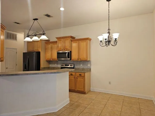 a kitchen with stainless steel appliances a chandelier a refrigerator a stove a microwave and cabinets