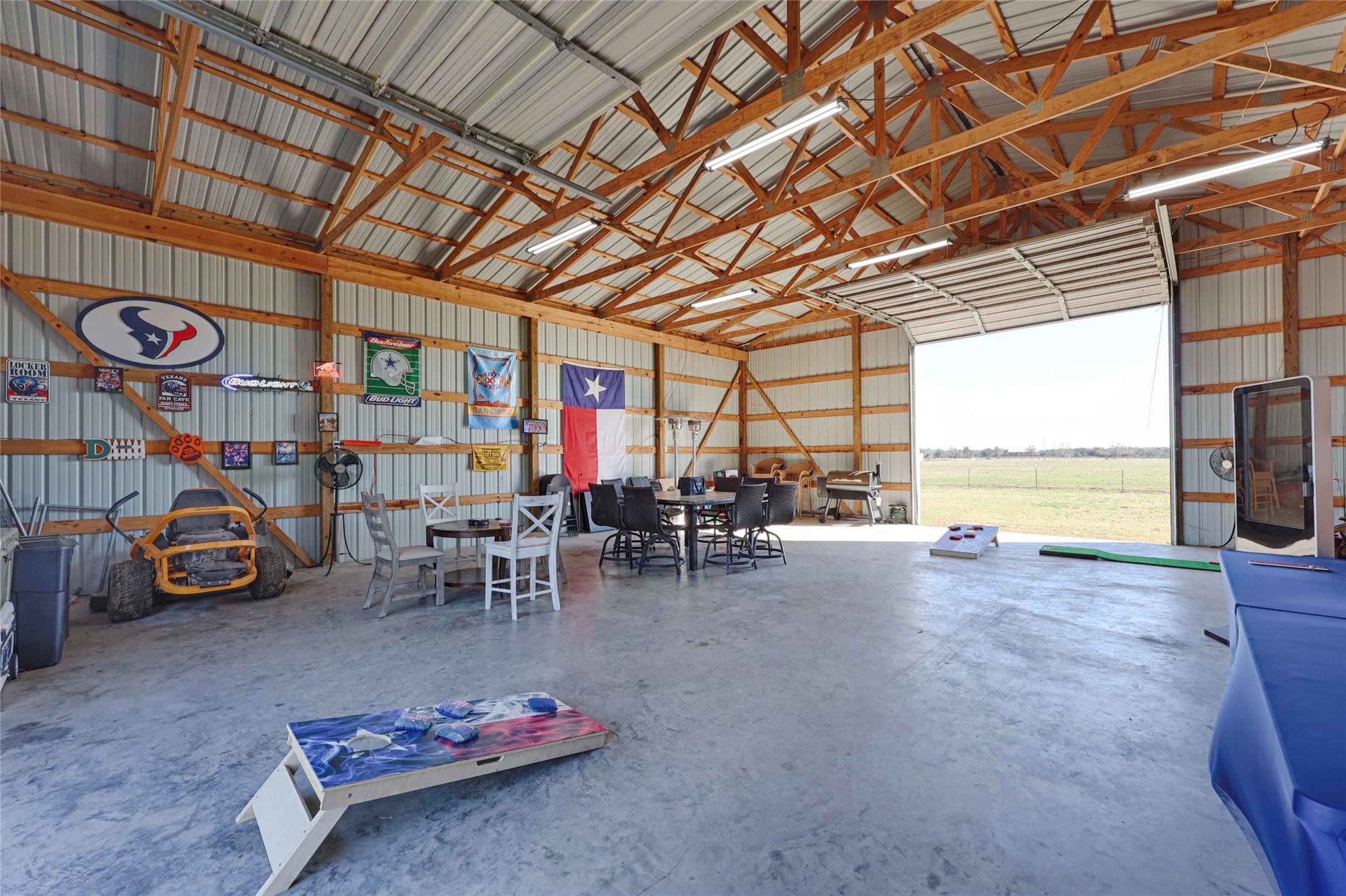 1055 County Road Weimar, TX 78962 - Photo 22 of 35 Spacious barn interior with open concrete floors, high ceilings, and roll-up door access. Well-suited for entertaining, workshop space, storage, or flexible use, offering a comfortable setup for gatherings and country hobbies alike. This barn includes a tack room, overhead storage and plenty of electrical outlets.