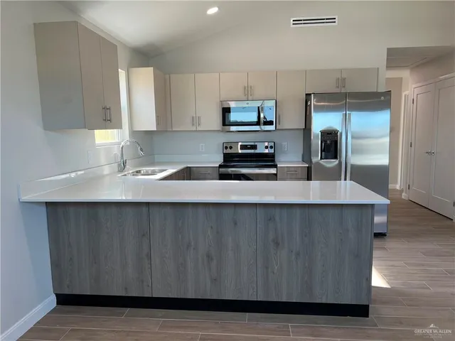 a kitchen with stainless steel appliances a sink a microwave a refrigerator and white cabinets