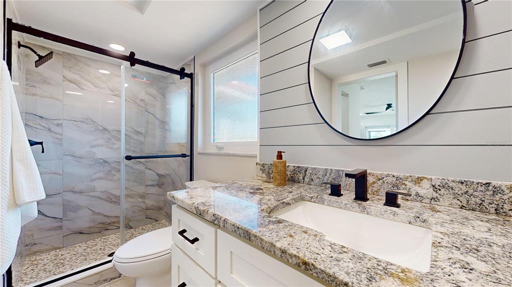 6380 3rd Palm Point St. Pete Beach, FL 33706 - Photo 29 of 48 a bathroom with a granite countertop sink a mirror a toilet and a shower