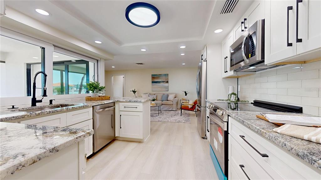 6380 3rd Palm Point St. Pete Beach, FL 33706 - Photo 9 of 48 an open kitchen with stainless steel appliances granite countertop a stove top oven a sink dishwasher a dining table and chairs with wooden floor