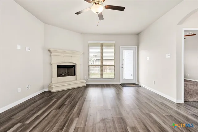 a view of an empty room with wooden floor fireplace and a window