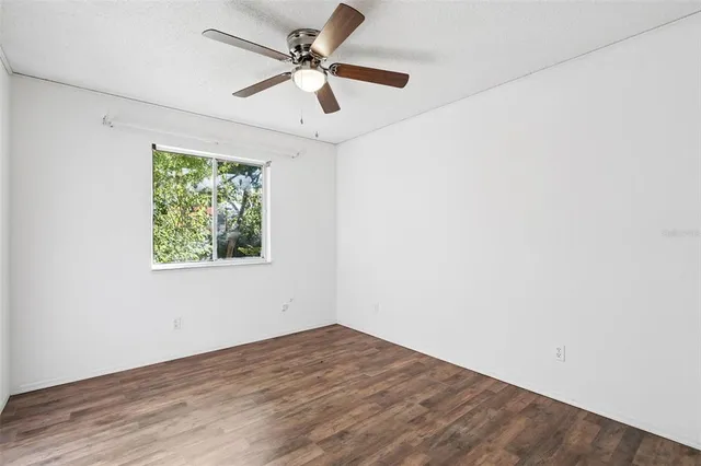 an empty room with wooden floor chandelier fan and windows