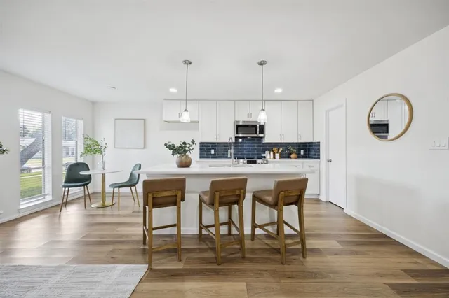 a kitchen with stainless steel appliances granite countertop a stove a refrigerator a kitchen island a dining table and chairs with wooden floor