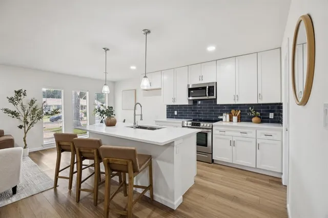 a kitchen with stainless steel appliances granite countertop a stove a sink a microwave a dining table and chairs with wooden floor