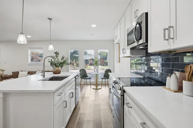 a open kitchen with stainless steel appliances granite countertop a sink dishwasher and white cabinets with wooden floor