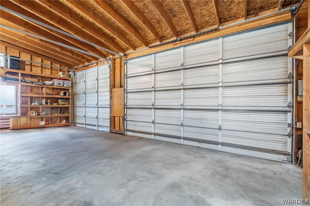 2401 North Stephan Road Kingman, AZ 86401 - Photo 68 of 92 Spacious garage featuring two sectional overhead doors, exposed wood beam ceiling, concrete flooring, built-in wooden shelving, and a side window