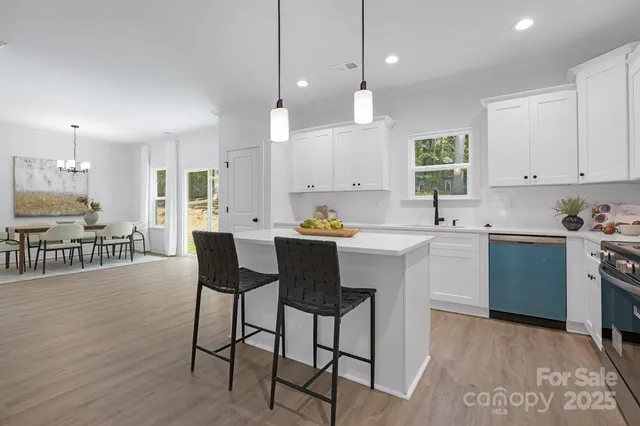 a kitchen that has a lot of cabinets in it with stainless steel appliances granite countertop a stove a sink a dining table and chairs with wooden floor