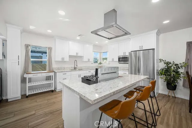 a kitchen with granite countertop a refrigerator a stove a sink and white cabinets with wooden floor