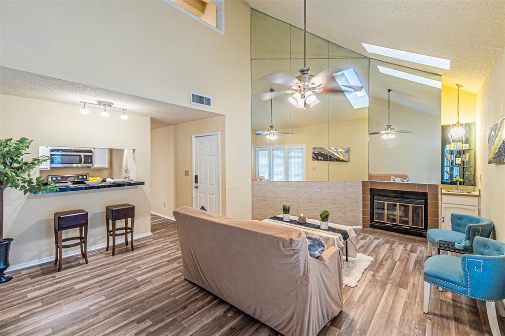 5590 Spring Valley Road, Unit C205 Dallas, TX 75254 - Photo 5 of 25 Living area featuring ceiling fan, lofted ceiling, wood finished floors, a tile fireplace, and a skylight