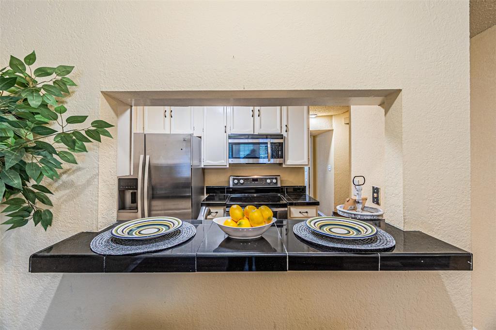 5590 Spring Valley Road, Unit C205 Dallas, TX 75254 - Photo 8 of 25 Kitchen featuring stainless steel appliances, dark countertops, a textured wall, white cabinets, and a peninsula