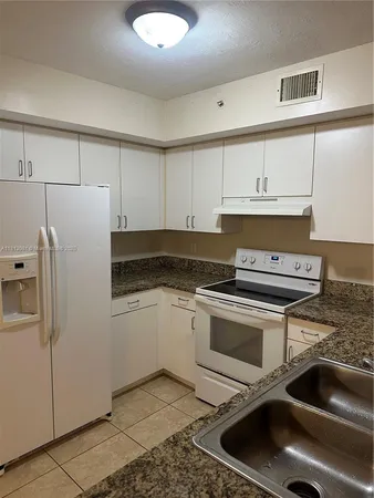 a kitchen with stainless steel appliances granite countertop a sink a stove a refrigerator and white cabinets