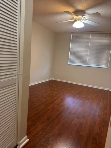 an empty room with wooden floor chandelier fan and windows