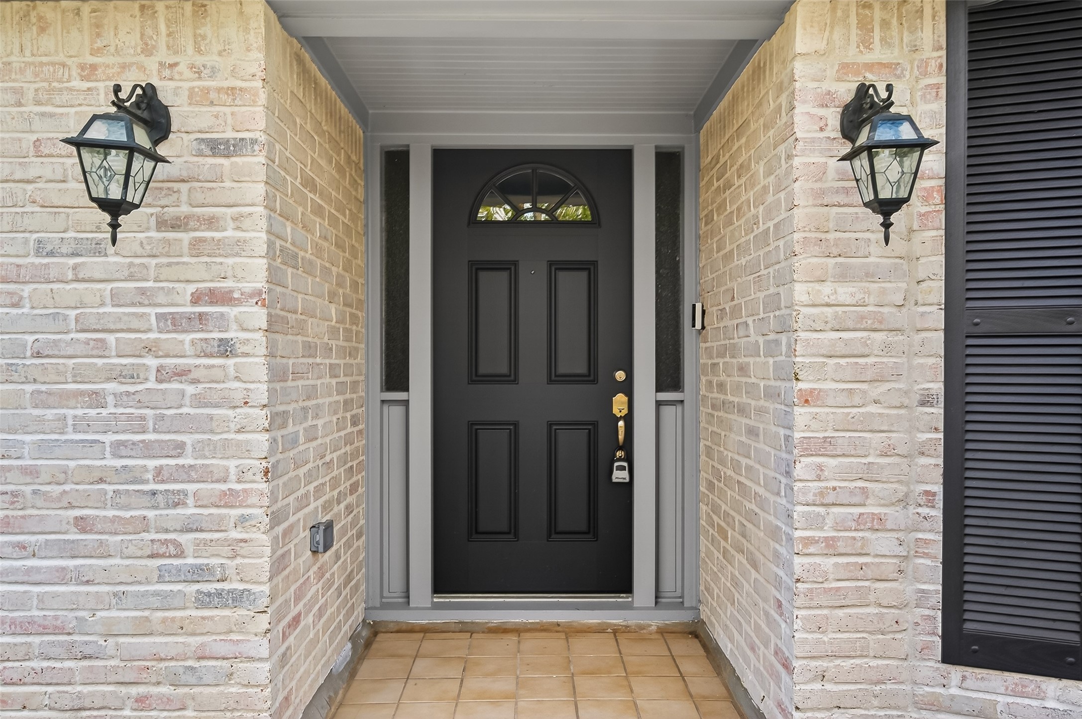 902 Kingsbridge Road Houston, TX 77073 - Photo 13 of 43 The exterior entry features a striking black front door with a semicircular transom window. It is framed by neutral-toned brick with a German Schmear finish, complemented by classic black shutters and traditional decorative wall lanterns that add to the home's curb appeal.