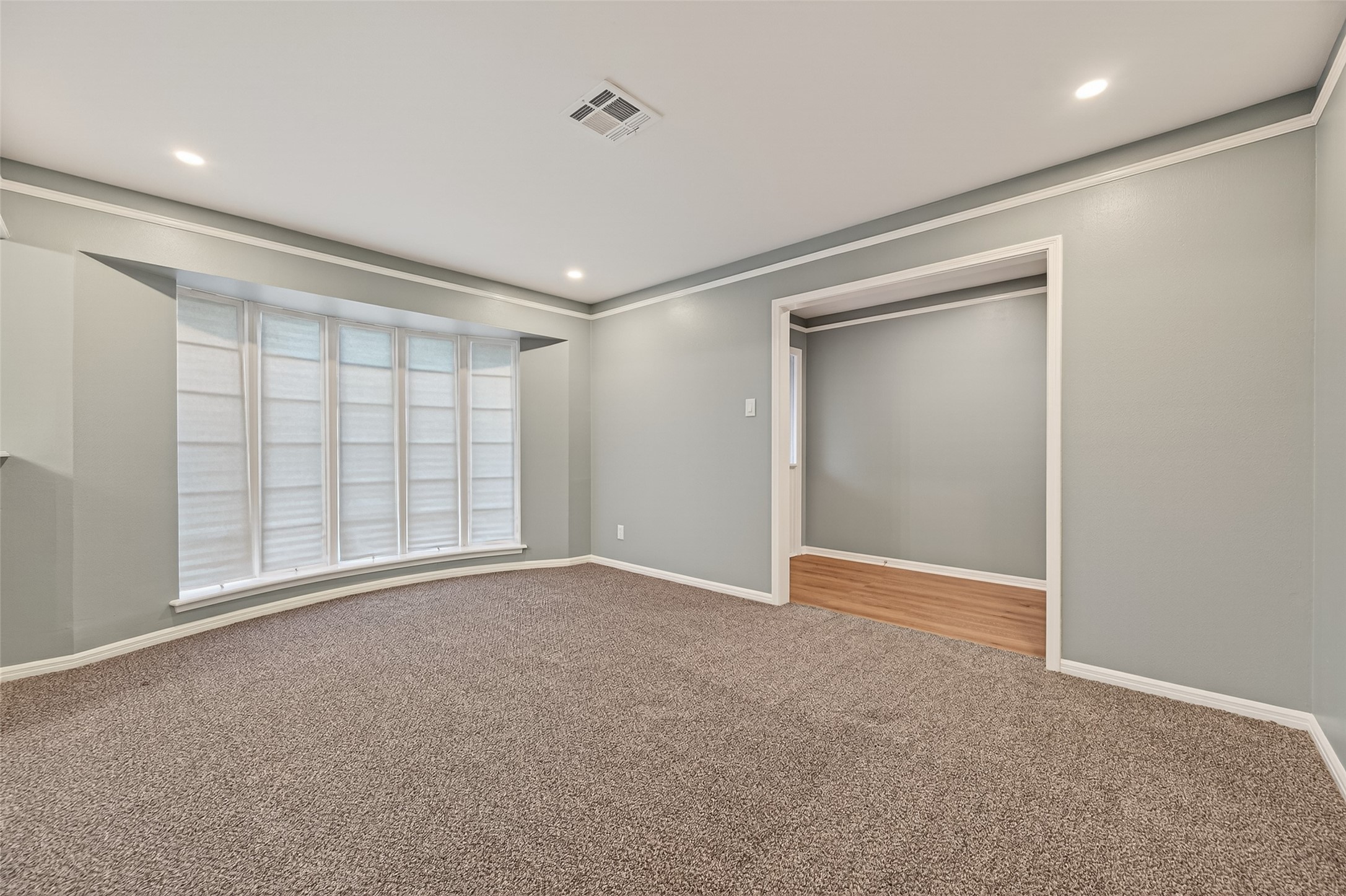 902 Kingsbridge Road Houston, TX 77073 - Photo 24 of 43 The formal living room is a bright and airy space featuring plush neutral carpeting and a large bay window that provides ample natural light. The room is finished with clean grey walls, crisp white crown molding, and recessed lighting, offering an open view into the adjacent foyer and dining areas.