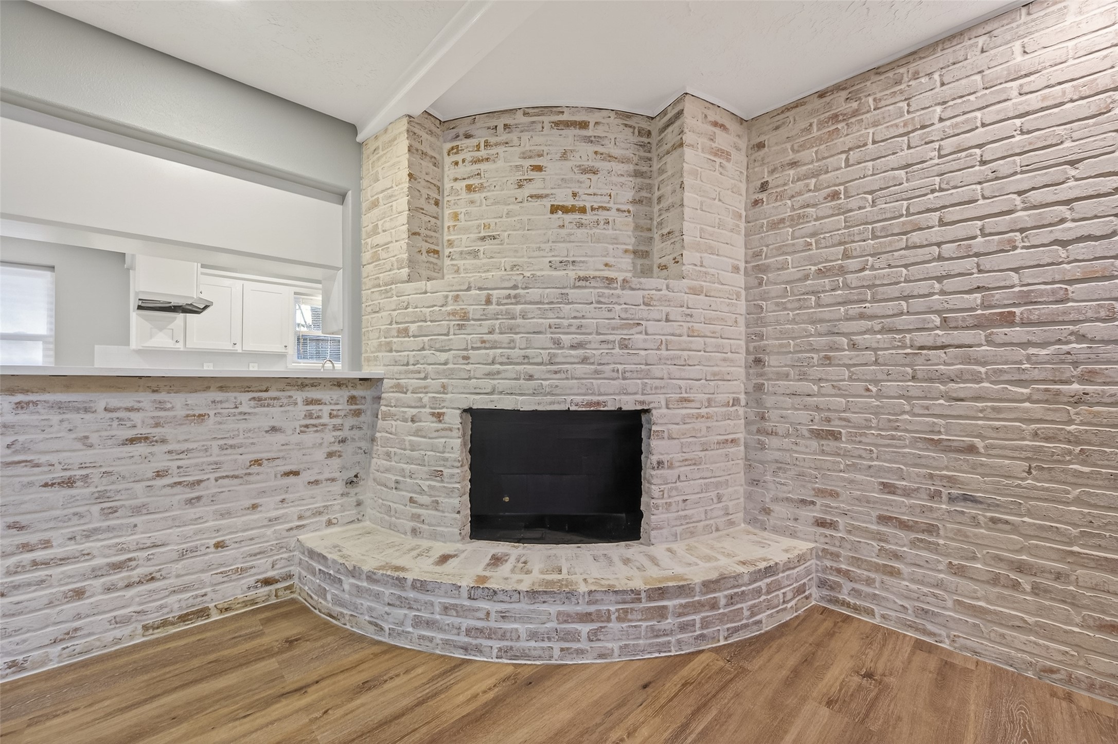 902 Kingsbridge Road Houston, TX 77073 - Photo 29 of 43 This striking floor-to-ceiling fireplace features a gas log set nestled within a classic brick hearth, beautifully finished with a textured German Schmear technique. The white-washed masonry adds a touch of rustic European charm, perfectly contrasting with the sleek wood-look flooring and modern neutral walls.