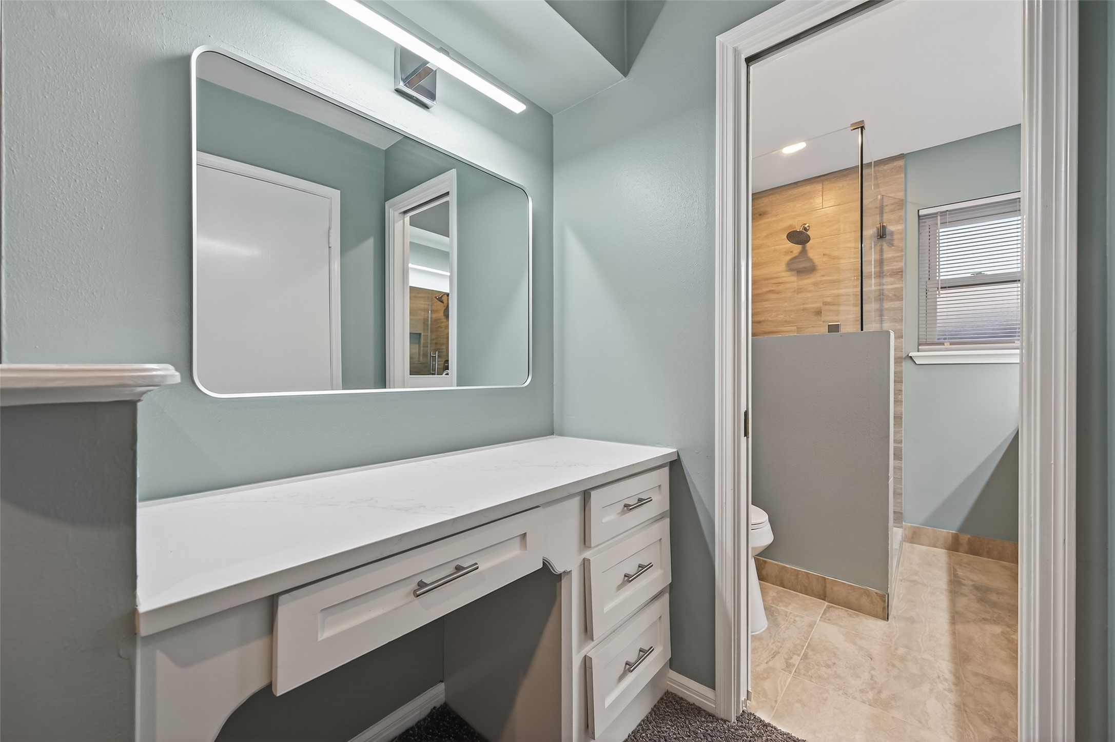 902 Kingsbridge Road Houston, TX 77073 - Photo 33 of 43 The primary bath features a long vanity with crisp white cabinetry, a dedicated seated makeup station, and brushed nickel hardware. The space is finished with a single large-format mirror that spans the length of the vanity, reflecting the room's bright, modern design.