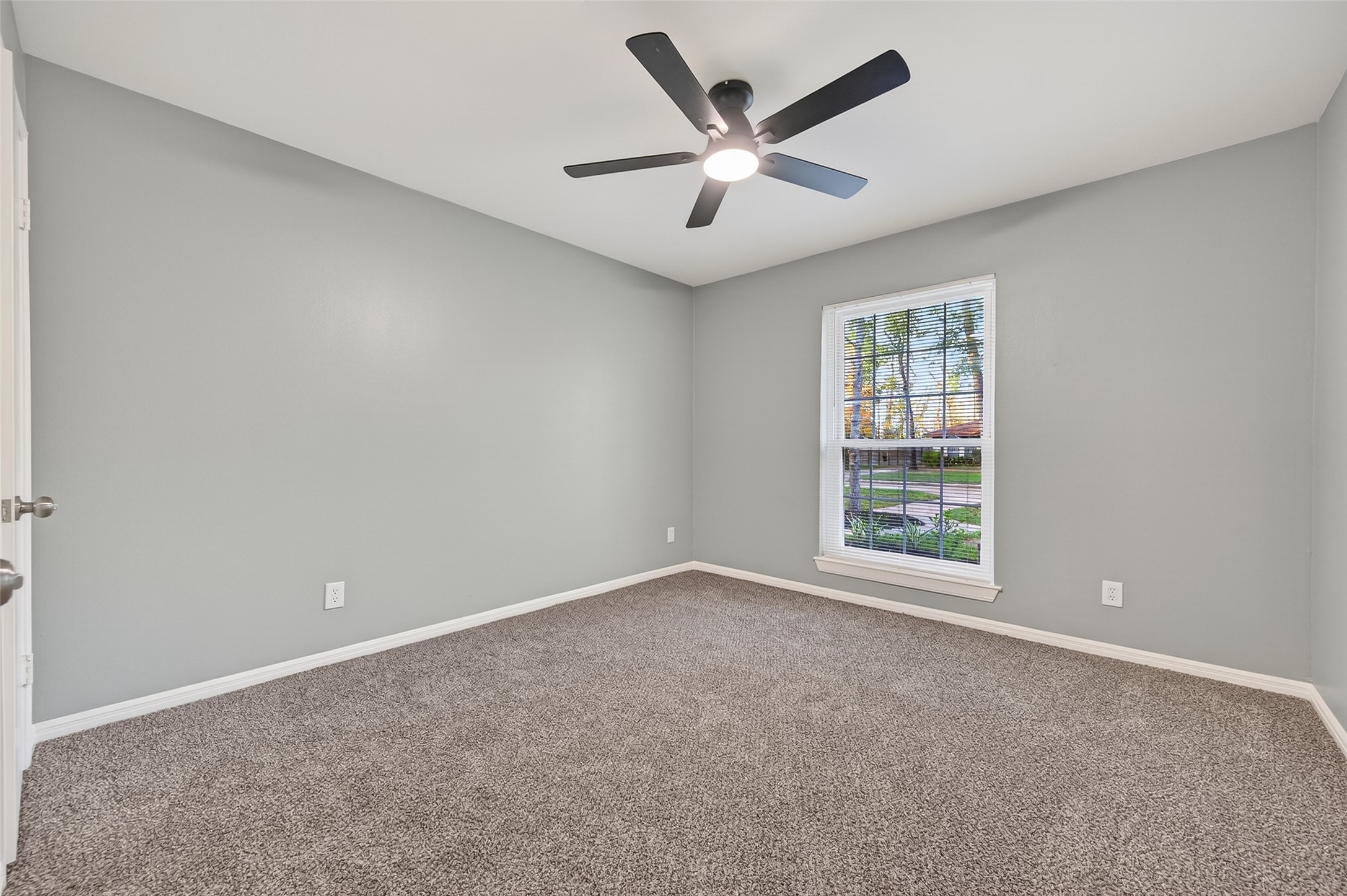902 Kingsbridge Road Houston, TX 77073 - Photo 37 of 43 The second bedroom is a comfortable and inviting space featuring plush neutral carpeting and a modern grey-toned color palette. A large window overlooks the outdoors, filling the room with natural light, while a contemporary black ceiling fan with an integrated light fixture provides both style and airflow.