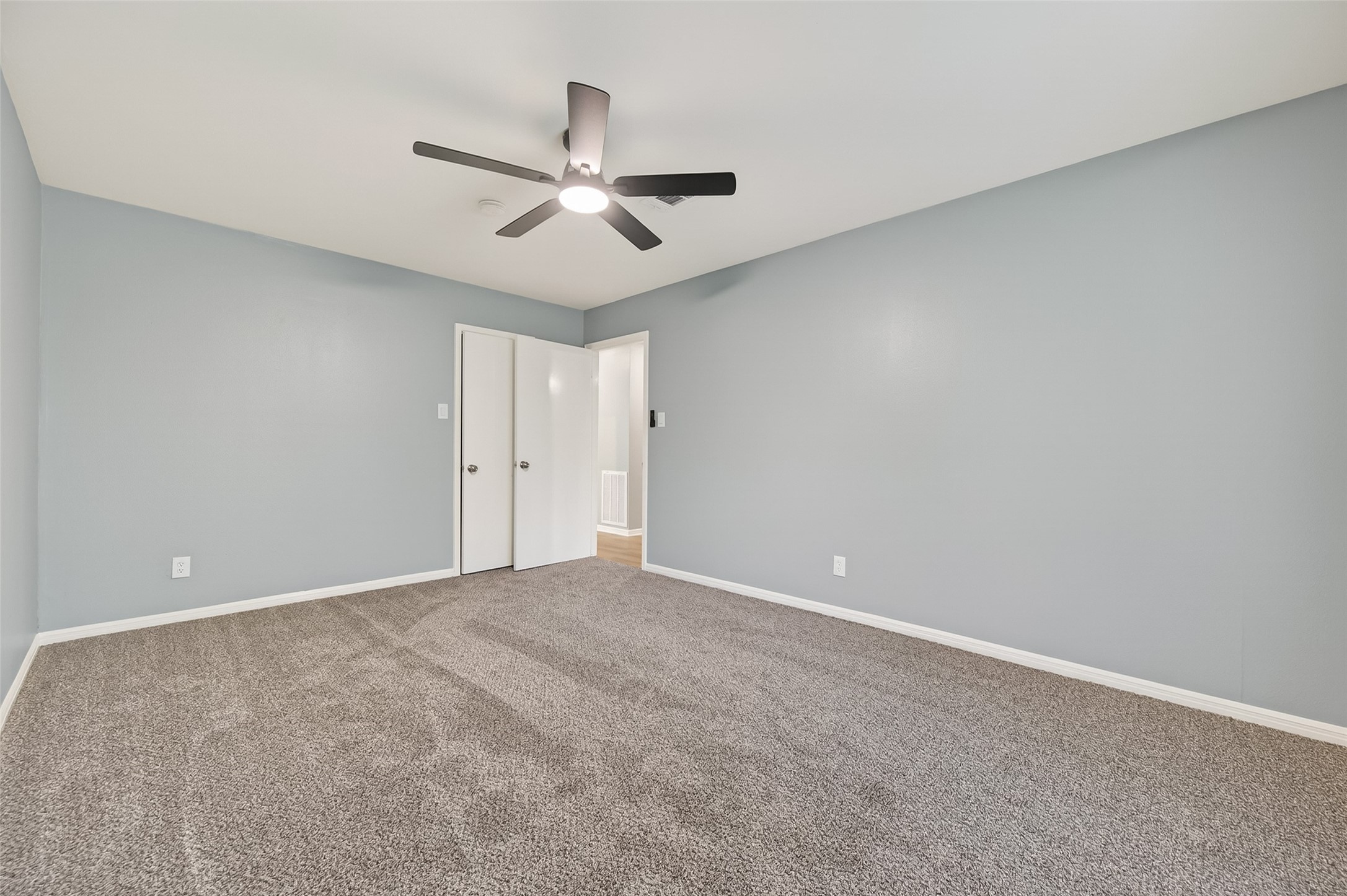 902 Kingsbridge Road Houston, TX 77073 - Photo 39 of 43 Bedroom 3 is a bright and spacious room featuring soft neutral carpeting and cool-toned grey walls. A modern black ceiling fan with an integrated light provides a stylish focal point, while the room's clean lines are accented by white baseboards and a matching closet door.