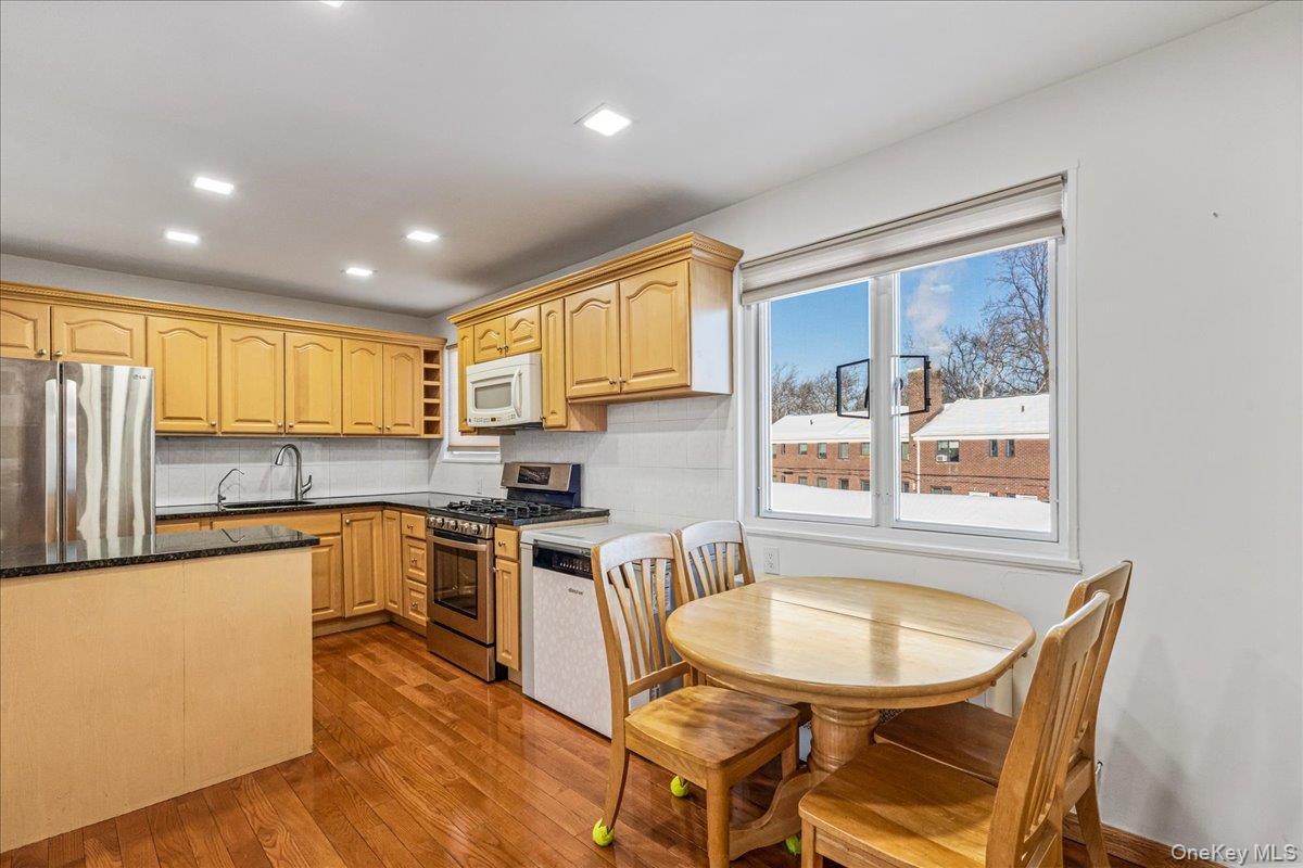 218-07 73rd Avenue, Unit UPPR Queens, NY 11364 - Photo 3 of 23 a kitchen with stainless steel appliances granite countertop a stove top oven a sink dishwasher a dining table and chairs with wooden floor