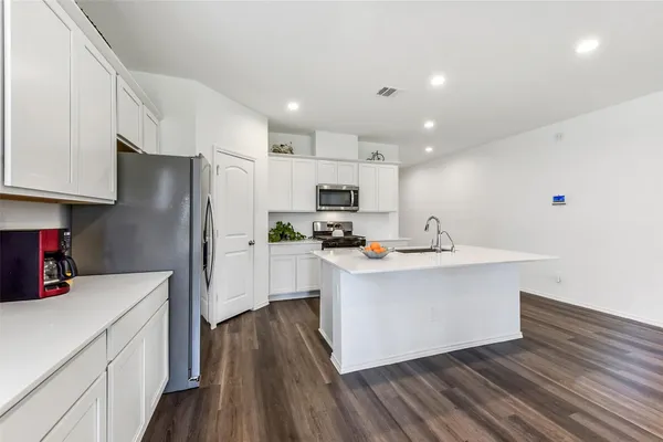 a kitchen with stainless steel appliances a refrigerator a sink dishwasher a stove and white cabinets with wooden floor