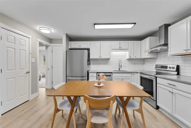 a kitchen with stainless steel appliances granite countertop a stove a refrigerator a sink dishwasher and white cabinets with wooden floor