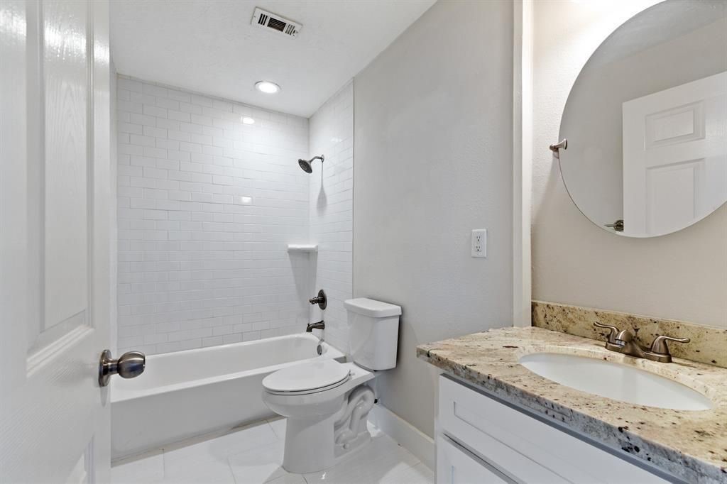 1305 Idylwild Street Houston, TX 77009 - Photo 13 of 31 This bathroom features a sleek design with a white subway tile shower, granite countertop, and modern fixtures. The neutral color palette and round mirror add a touch of elegance.