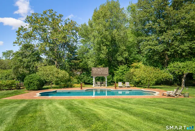 a view of a swimming pool with lawn chairs and large trees