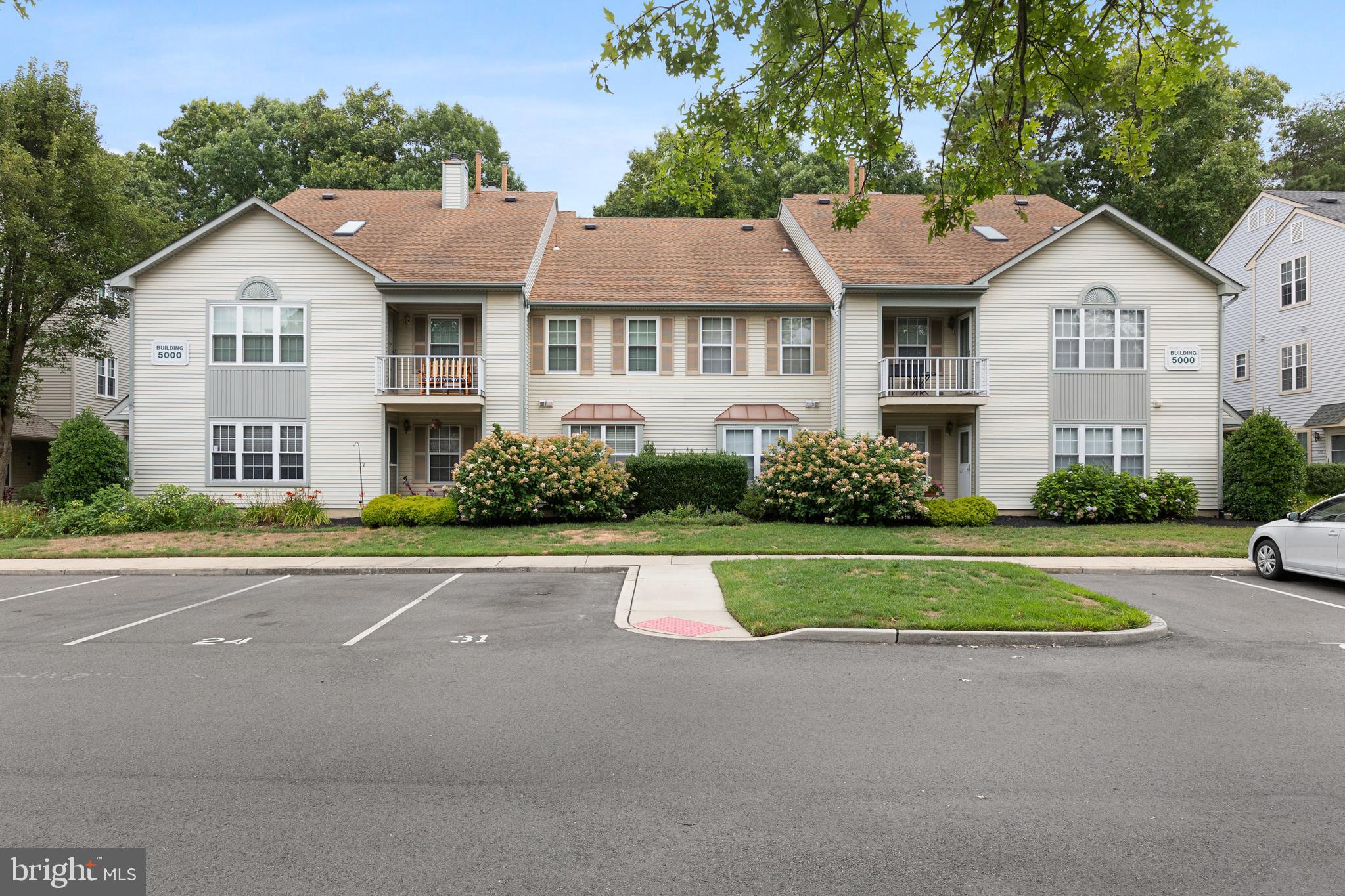 a view of a white house with a yard plants and large tree