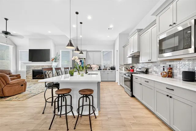 a kitchen with stainless steel appliances kitchen island granite countertop a stove top oven a sink dishwasher and a dining table with wooden floor