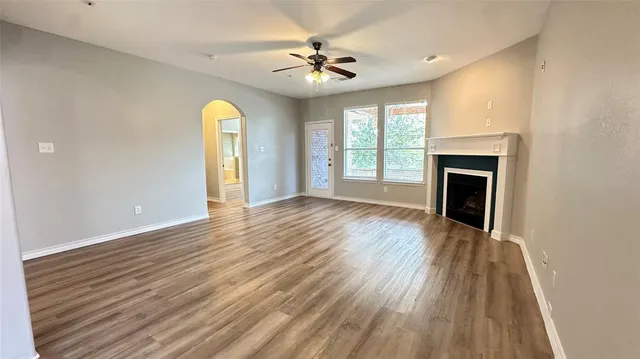 a view of an empty room with wooden floor fireplace and a window