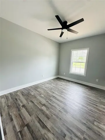 an empty room with wooden floor ceiling fan and windows