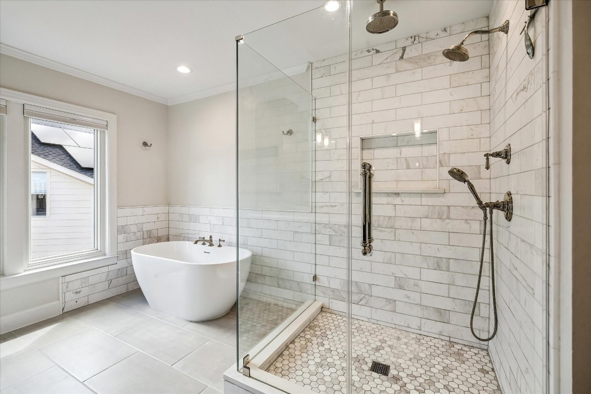 1925 Banks Street Houston, TX 77098 - Photo 21 of 38 This bathroom features a modern design with a freestanding soaking tub and a spacious glass-enclosed shower. The walls are adorned with white subway tiles, while the floor features elegant hexagonal tiles. A large window provides natural light, creating a bright and serene space.