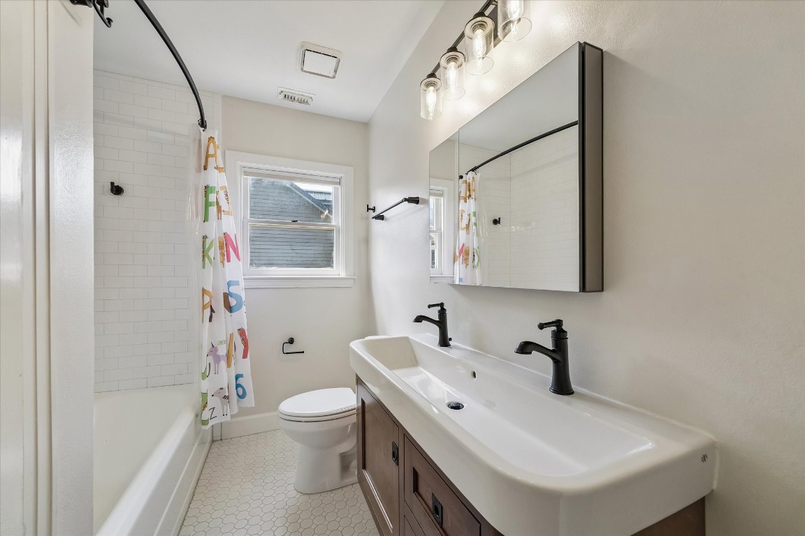 1925 Banks Street Houston, TX 77098 - Photo 26 of 38 Bright, modern bathroom featuring a double sink vanity with black fixtures, a shower-tub combo with tiled walls, and a window for natural light.