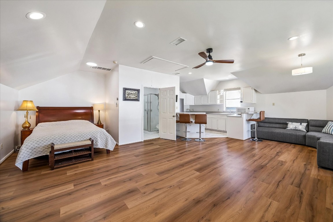 1925 Banks Street Houston, TX 77098 - Photo 30 of 38 This spacious, open-plan room features warm wood flooring, a cozy sleeping area with a bed, a modern kitchen with white cabinetry, a breakfast bar with seating, and a comfortable living space with a sectional sofa. Ideal for a multifunctional living setup.