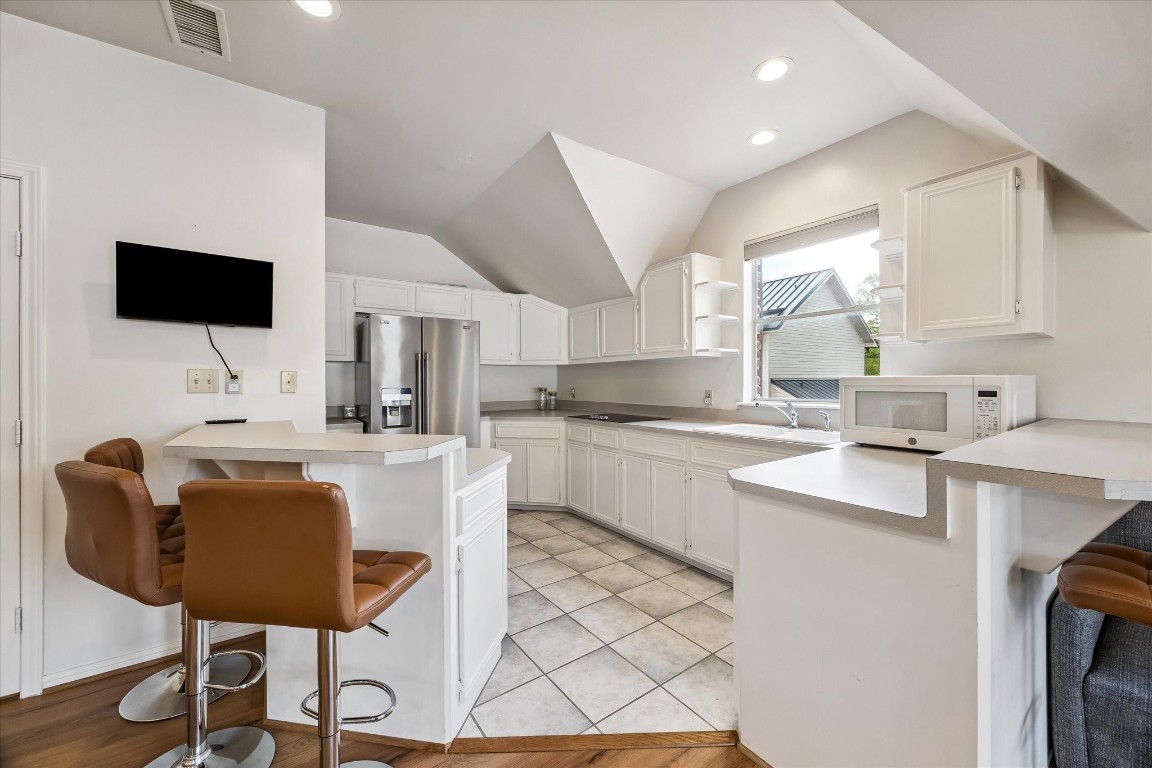 1925 Banks Street Houston, TX 77098 - Photo 32 of 38 This kitchen features a clean design with white cabinetry, a stainless steel fridge, and ample counter space. It includes a breakfast bar with room for four to five barstools and large windows for natural light. The space combines tile and wood flooring for a contemporary look.