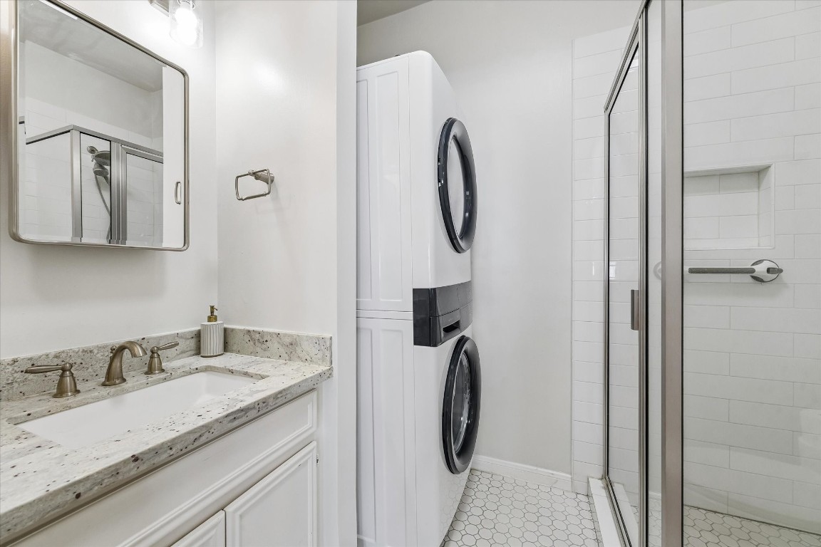 1925 Banks Street Houston, TX 77098 - Photo 33 of 38 Modern remodeled bathroom featuring a granite countertop with a sink, a new stacked washer and dryer, and a glass-enclosed shower. The space is bright and efficiently designed.