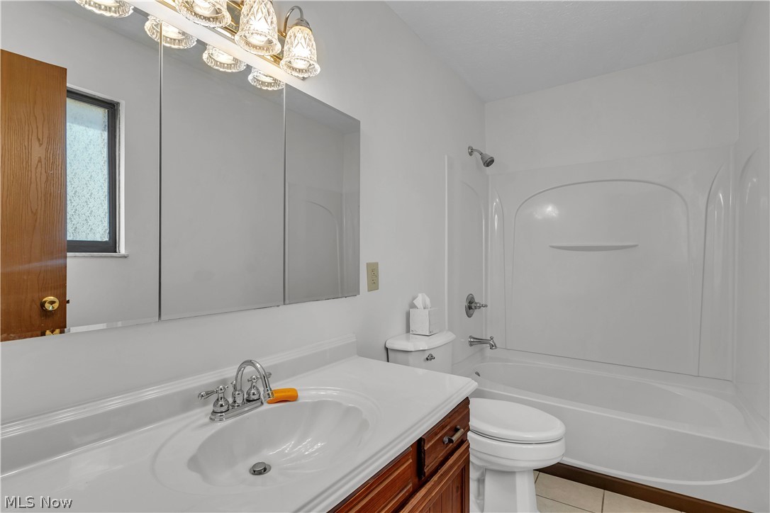 6635 Taylor Road Painesville, OH 44077 - Photo 28 of 41 Second Floor Full bathroom featuring a single vanity with a white countertop and wood-finish cabinetry, a three-section mirrored medicine cabinet, a full bathtub with an integrated shower, and a window with privacy glass