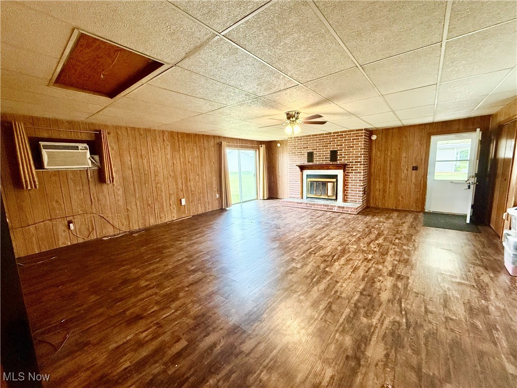 923 Archer Hill Road Colliers, WV 26035 - Photo 8 of 33 Unfurnished living room with wood walls, wood finished floors, a fireplace, a wall unit AC, and ceiling fan