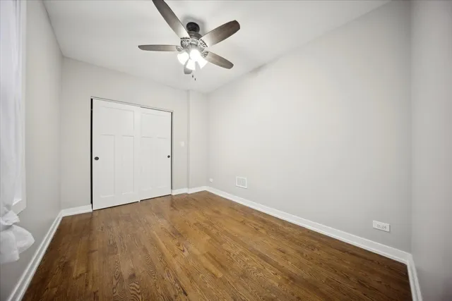 an empty room with a chandelier fan and wooden floor