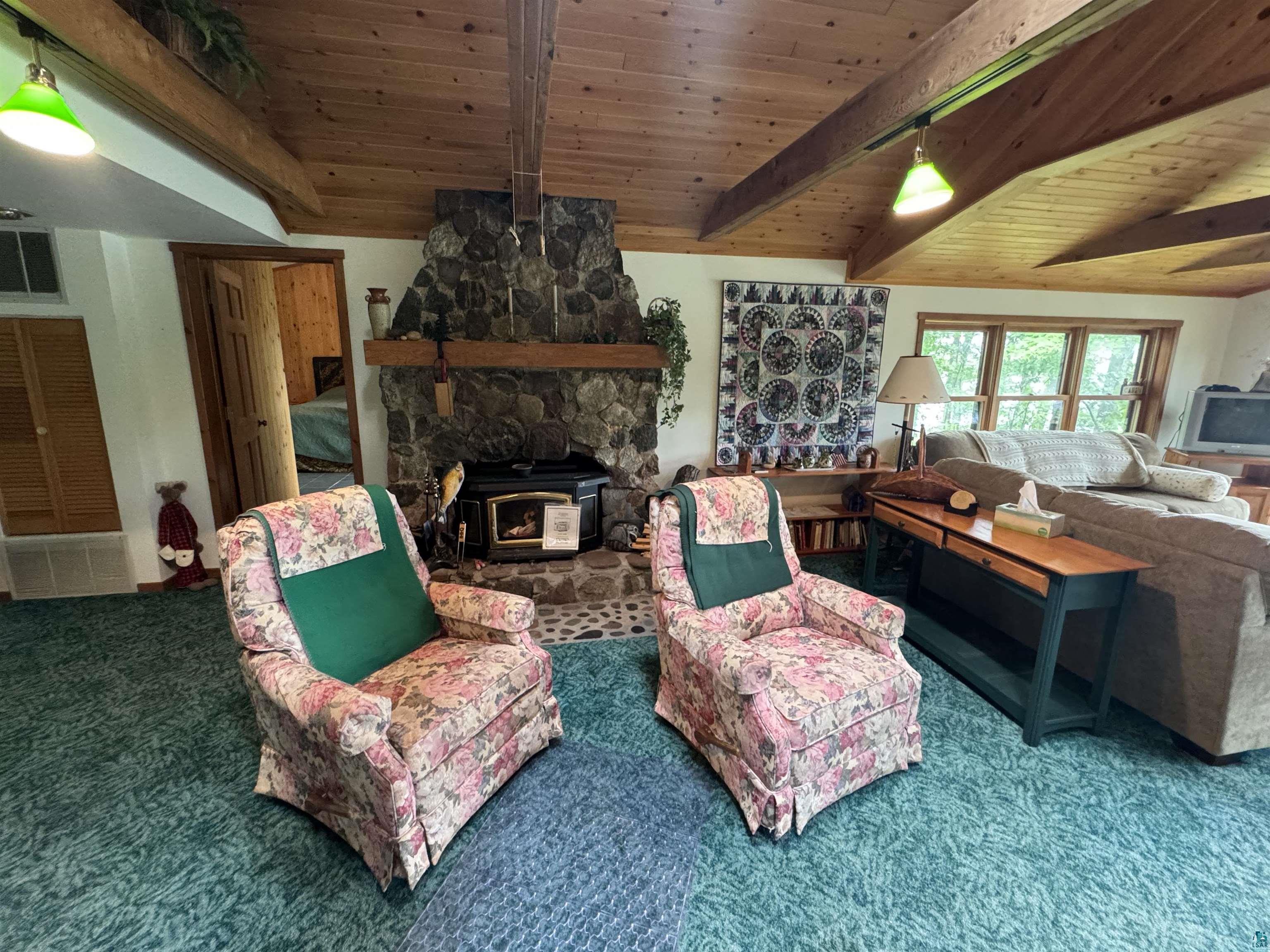 10690 Cedar Crest Road Iron River, WI 54847 - Photo 13 of 24 Living room with vaulted ceiling with beams, a wood burning fireplace, carpet, and wooden ceiling