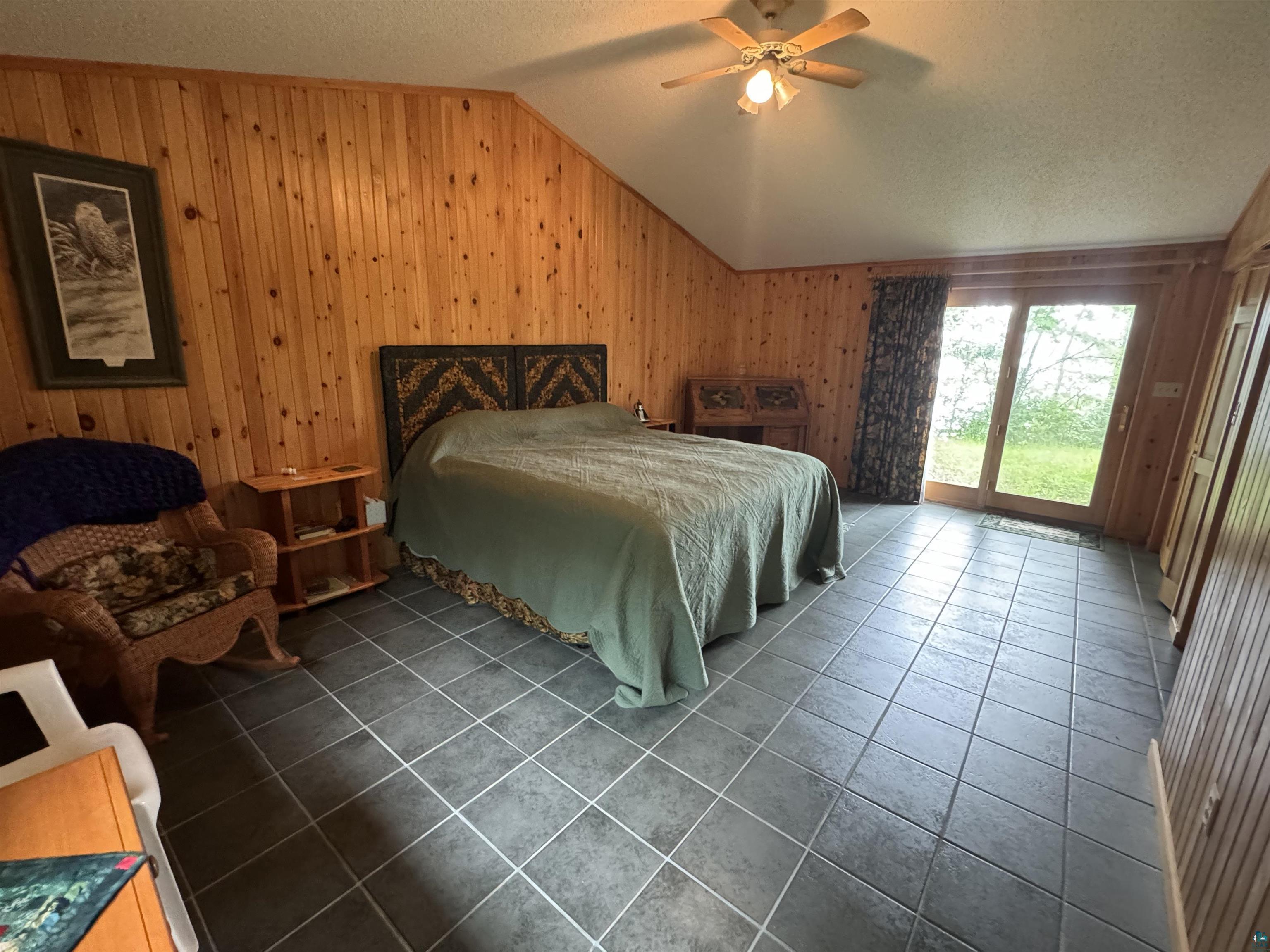 10690 Cedar Crest Road Iron River, WI 54847 - Photo 16 of 24 Tiled bedroom with ceiling fan, vaulted ceiling, a textured ceiling, access to exterior, and wood walls