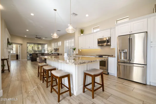 a kitchen with stainless steel appliances kitchen island granite countertop a refrigerator a stove a microwave oven a dining table and chairs with wooden floor