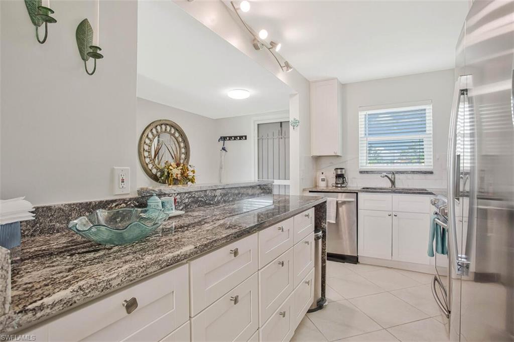 4380 27th Court Southwest, Unit 1 Naples, FL 34116 - Photo 12 of 34 Kitchen with appliances with stainless steel finishes, white cabinetry, light tile patterned flooring, and dark stone countertops