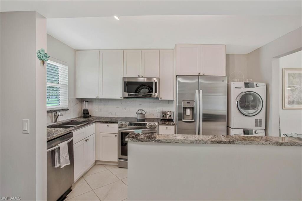 4380 27th Court Southwest, Unit 1 Naples, FL 34116 - Photo 6 of 34 Kitchen with appliances with stainless steel finishes, dark stone look countertops, tasteful backsplash, washer dryer in unit