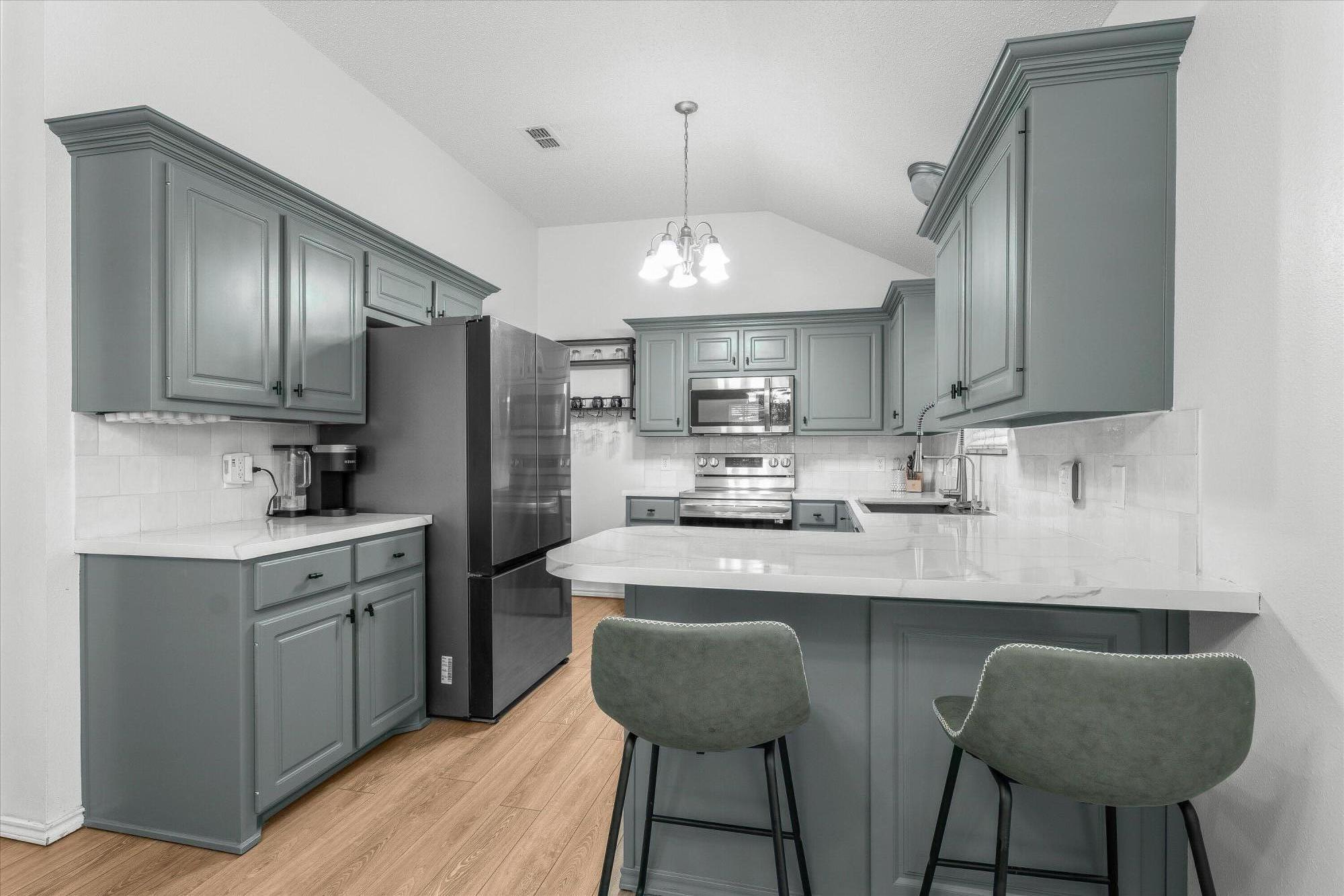 a kitchen with stainless steel appliances granite countertop a sink a stove a refrigerator cabinets and chairs