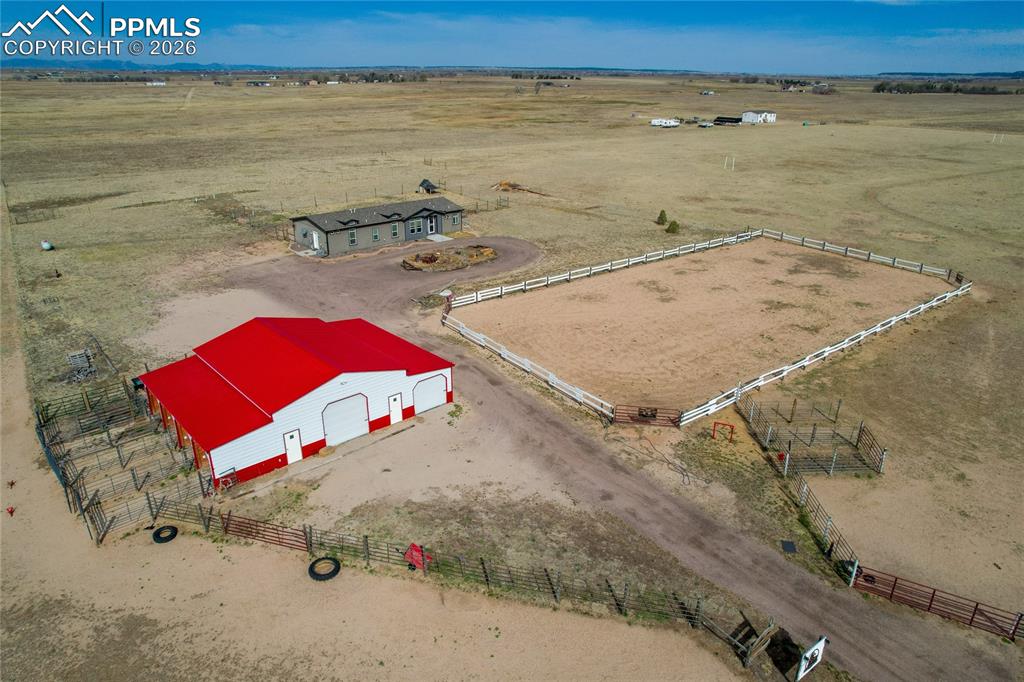 7880 J D Johnson Road Peyton, CO 80831 - Photo 19 of 50 Expansive property featuring a red and white barn with multiple garage doors, a fenced riding arena, and a single-story dwelling