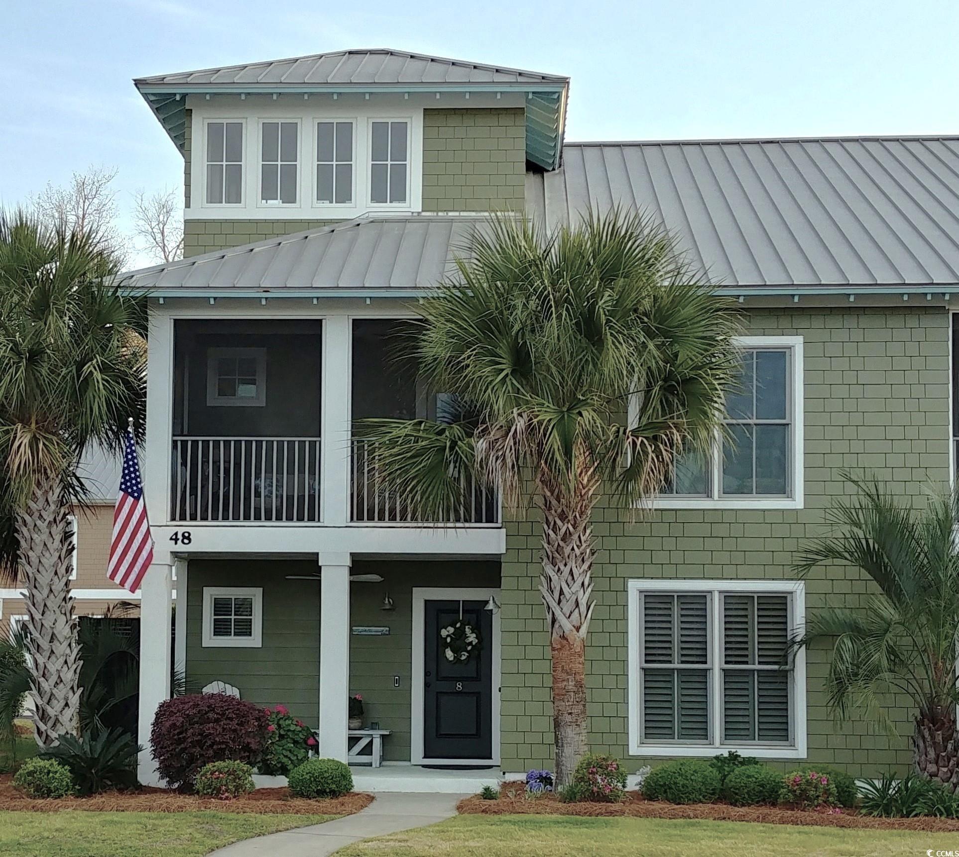 View of front facade with a standing seam roof, a metal roof, covered porch, a balcony, and a front lawn