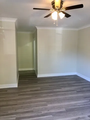 a view of an empty room with wooden floor and a ceiling fan